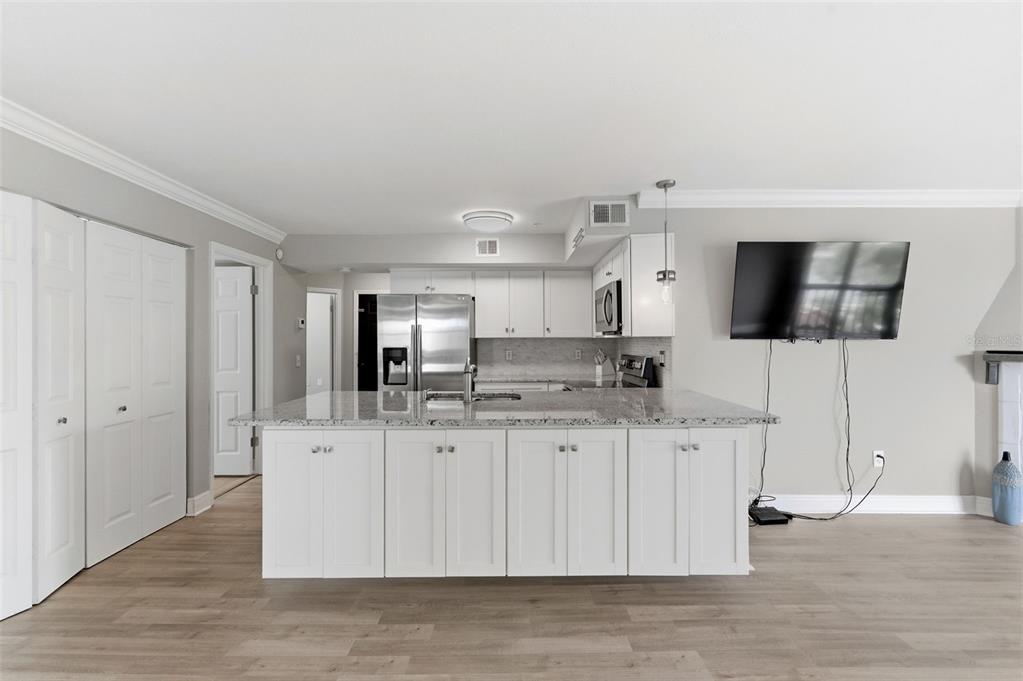 A kitchen features white cabinets, a granite-topped island, stainless steel appliances, and wood-look flooring — 2400 FEATHER SOUND DRIVE UNIT 1136, CLEARWATER, FL