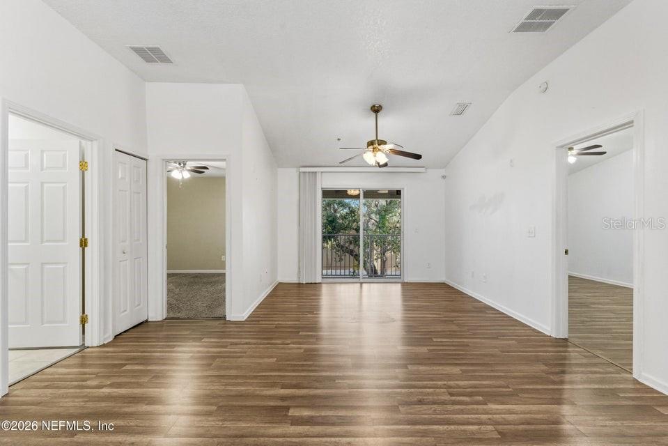 An empty living room features wood-look flooring, a vaulted ceiling, and a sliding glass door — 7047 DEER LODGE CIRCLE UNIT 108, JACKSONVILLE, FL