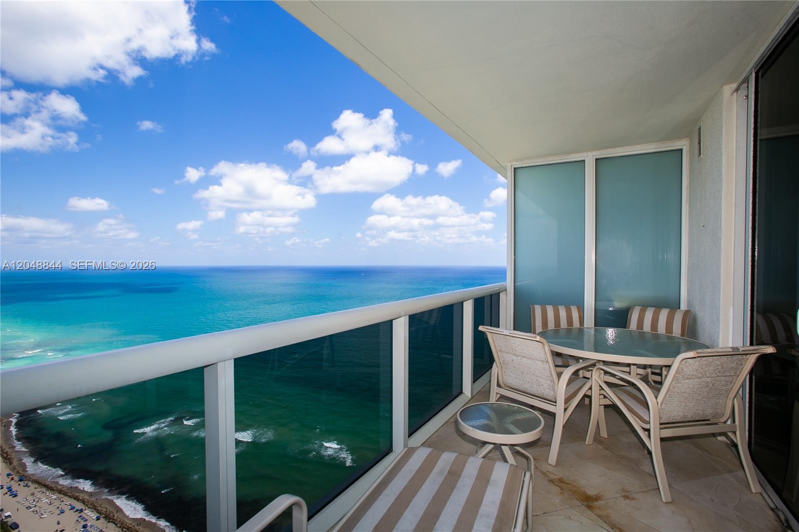 A balcony with outdoor furniture overlooks the ocean under a blue sky with clouds — 1830 S Ocean Dr # 4812, Hallandale Beach FL 33009, HALLANDALE BEACH, FL