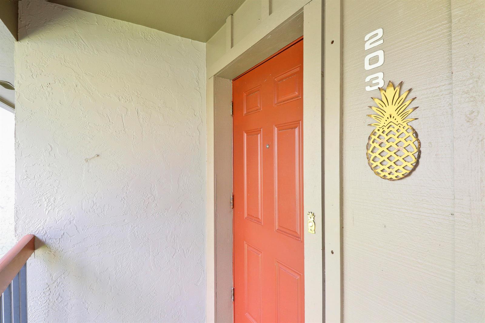An orange front door with a pineapple decoration and the number 303 on the wall — 1600 NE Dixie Highway # 203, Jensen Beach FL 34957, JENSEN BEACH, FL
