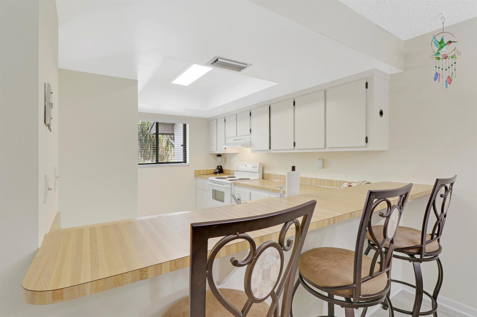 A kitchen features white cabinets, a light wood countertop breakfast bar, and two metal chairs — 1600 NE Dixie Highway # 203, Jensen Beach FL 34957, JENSEN BEACH, FL