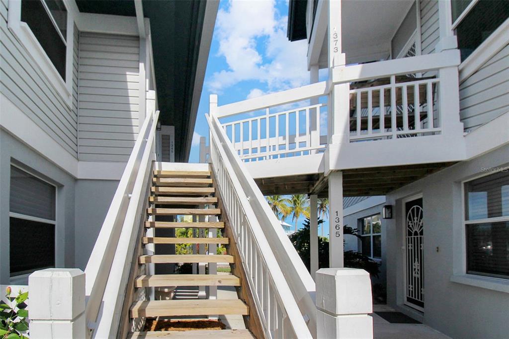 An exterior view of a wooden staircase leading up to a balcony between two buildings — 1373 SIESTA BAYSIDE DRIVE UNIT 1373-C, SARASOTA, FL