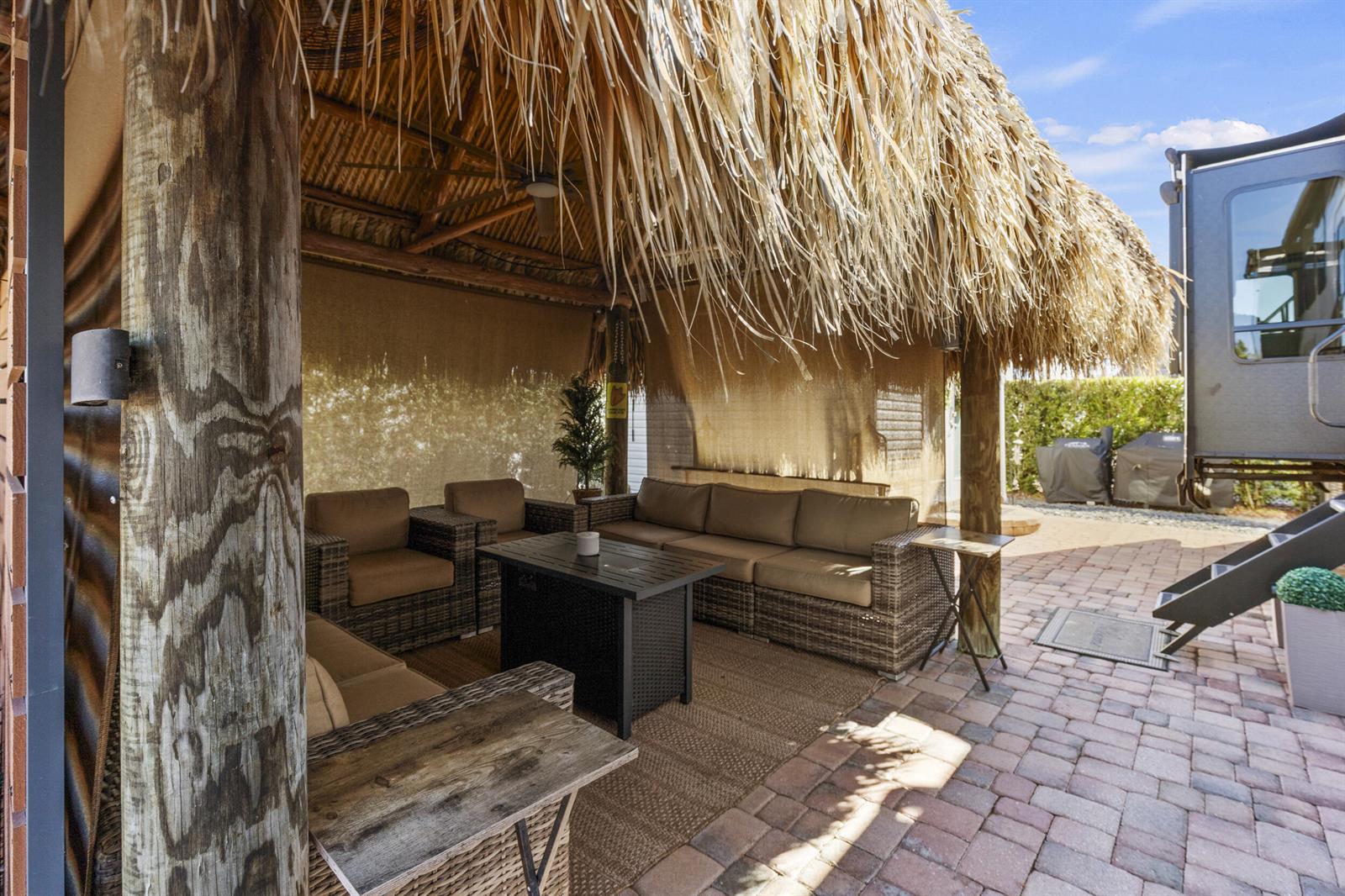 A thatched-roof tiki hut covers an outdoor patio with wicker furniture and a fire table — 532 SW 38th Trace, Okeechobee FL 34974, OKEECHOBEE, FL