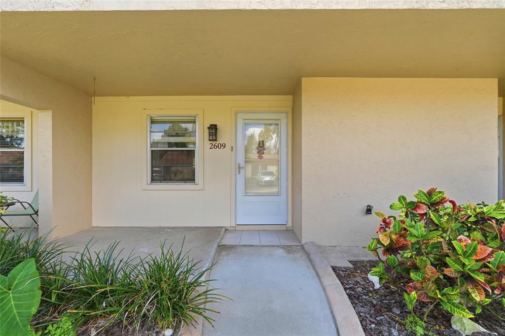 A beige exterior wall features a front door, a window, and a concrete walkway — 2609 WOODGATE LANE UNIT K4, SARASOTA, FL