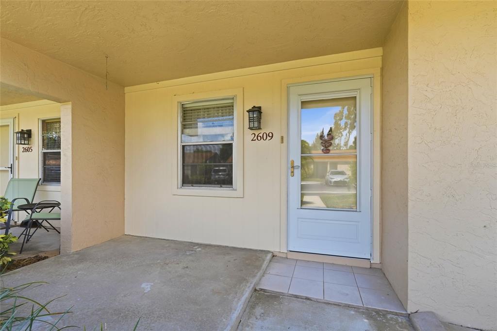 A covered concrete porch features a front door with a storm door and a window — 2609 WOODGATE LANE UNIT K4, SARASOTA, FL