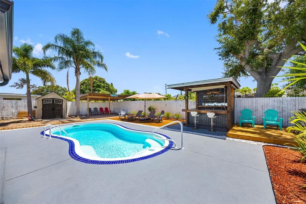 A backyard features a swimming pool, a tiki bar, a shed, and lounge seating — 1036 VIKING DRIVE, HOLIDAY, FL