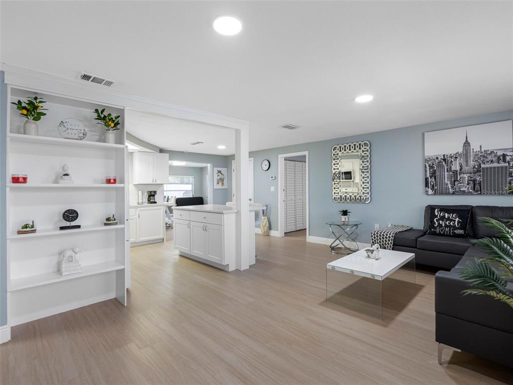 A living room with light wood floors, a white bookshelf, and a grey sofa — 1036 VIKING DRIVE, HOLIDAY, FL