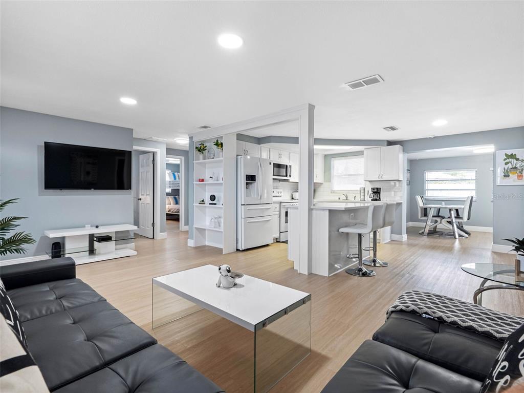 An open-concept living room and kitchen featuring light wood flooring and modern white cabinetry — 1036 VIKING DRIVE, HOLIDAY, FL