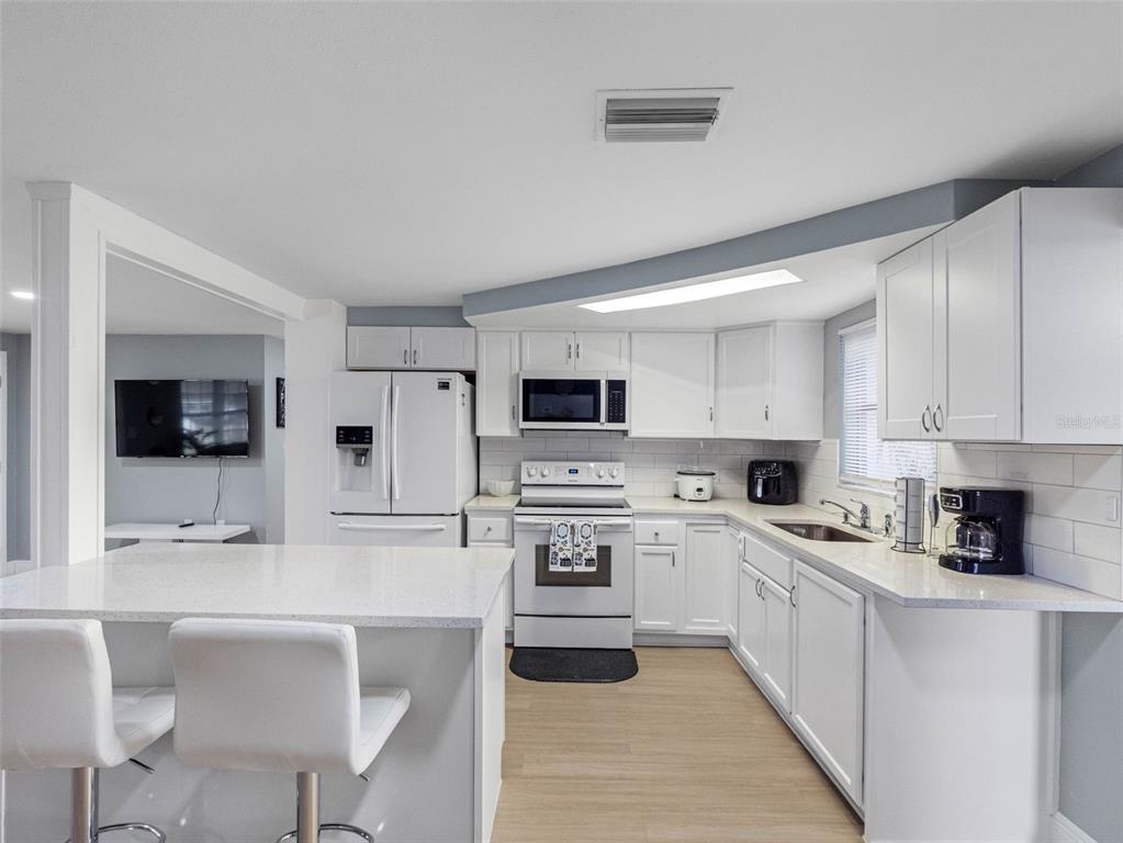 A white kitchen features a breakfast bar, quartz countertops, and stainless steel appliances — 1036 VIKING DRIVE, HOLIDAY, FL
