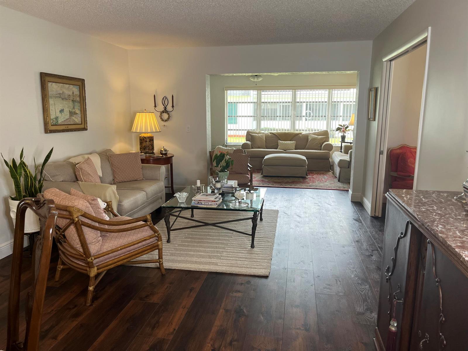 A living room with dark wood floors, a glass coffee table, and a sunroom beyond — 2638 Gately Drive E # 112, West Palm Beach FL 33415, WEST PALM BEACH, FL
