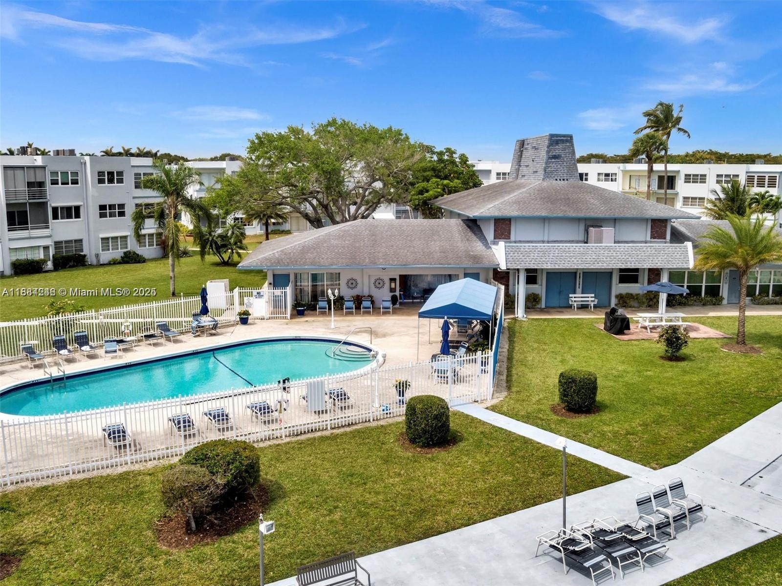 An outdoor swimming pool is surrounded by a white fence, patio furniture, and grassy lawns — 2300 Park Ln # 211, Hollywood FL 33021, HOLLYWOOD, FL