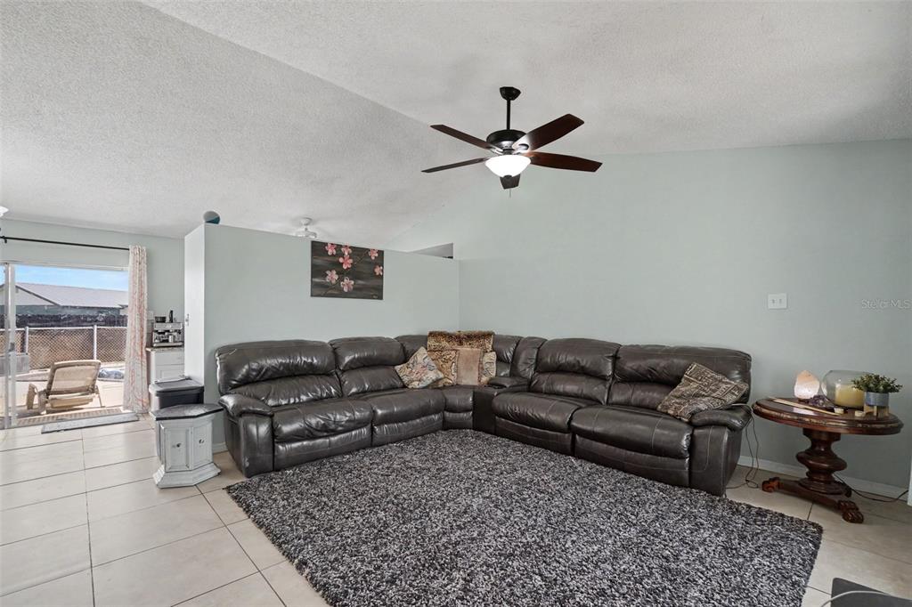 A living room features a large dark leather sectional, a gray rug, and a ceiling fan — 13238 FOWLER AVE, PORT CHARLOTTE, FL