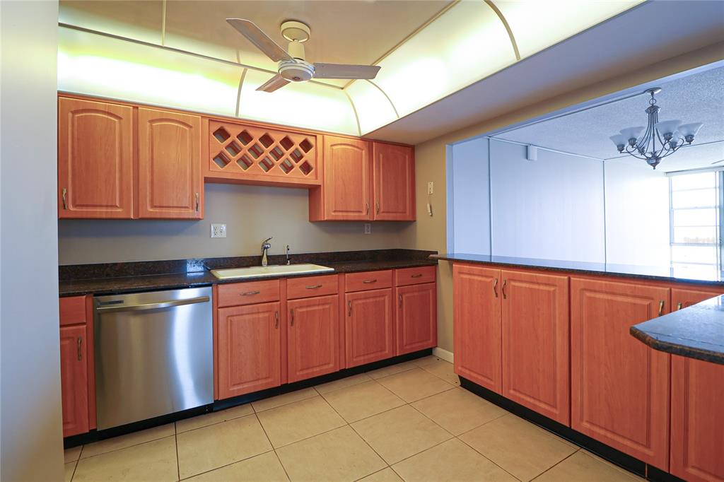 A kitchen features wood cabinets, dark granite countertops, stainless steel appliances, and tile flooring — 7400 SUN ISLAND DRIVE S UNIT 501, SOUTH PASADENA, FL