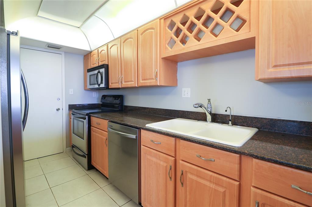 A kitchen features light wood cabinets, dark countertops, a white double sink, and stainless appliances — 7400 SUN ISLAND DRIVE S UNIT 501, SOUTH PASADENA, FL