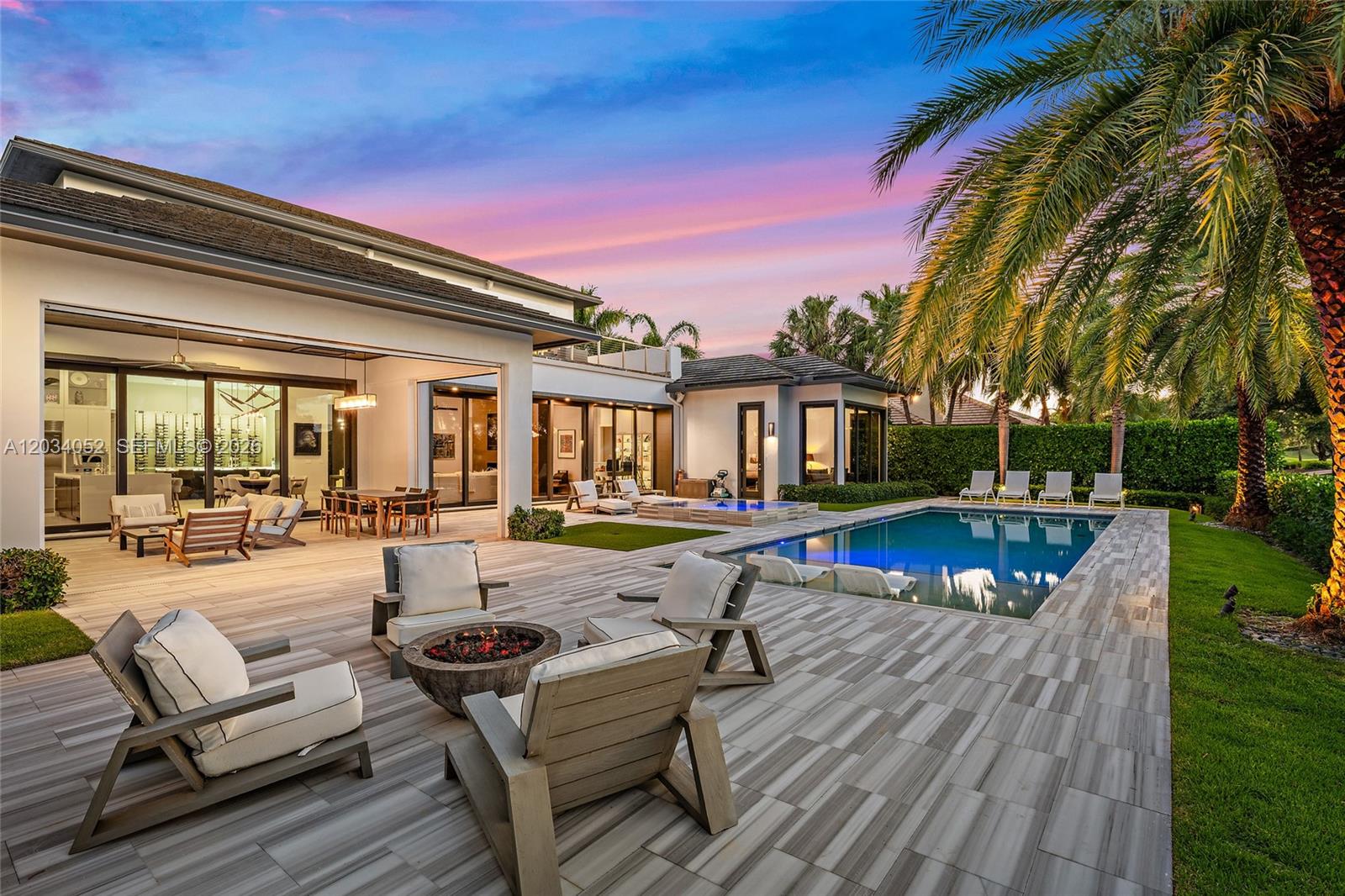 A modern patio with a fire pit, lounge seating, and a swimming pool at sunset — 162 Commodore Dr, Jupiter FL 33477, JUPITER, FL