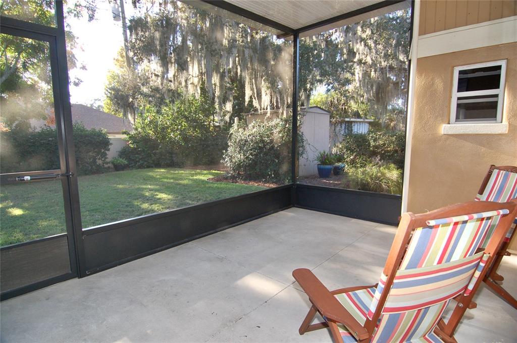 A screened-in concrete patio features two striped wooden chairs and a view of the backyard — 1940 SUNSET LANE, CLERMONT, FL