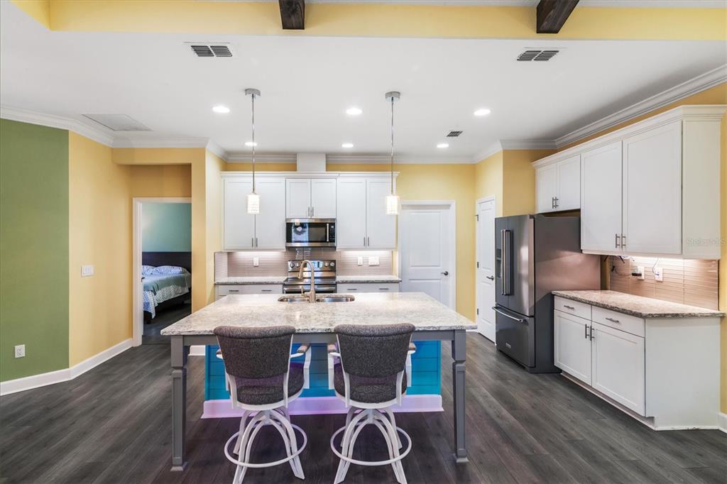 A kitchen features white cabinets, a granite-topped island with teal accents, and dark wood flooring — 485 MARGARITAVILLE AVENUE, DAYTONA BEACH, FL