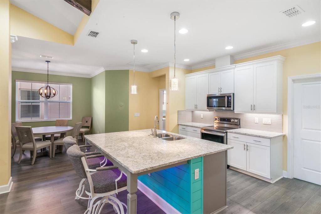 A kitchen with white cabinets, a granite-topped island, and a dining area with green walls — 485 MARGARITAVILLE AVENUE, DAYTONA BEACH, FL