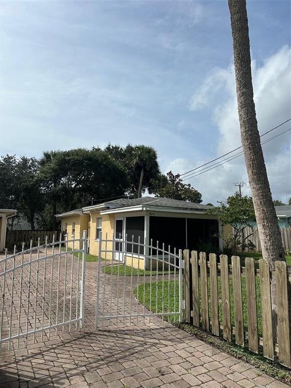A yellow house with a screened-in porch sits behind a white metal gate — 401 OAKWOOD AVENUE UNIT A, NEW SMYRNA BEACH, FL