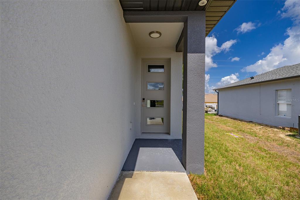 A modern front door with four rectangular glass panels sits under a covered entryway — 804-806 COLVILLE DRIVE, KISSIMMEE, FL