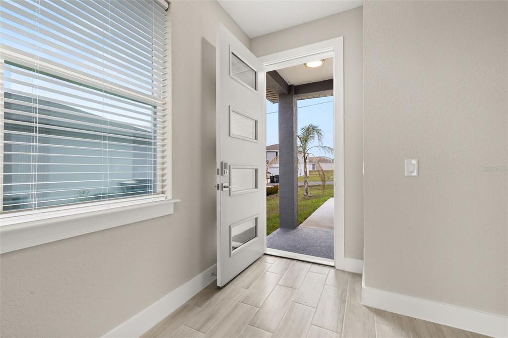 An entryway with light-colored tile flooring features an open white door leading to a porch — 804-806 COLVILLE DRIVE, KISSIMMEE, FL
