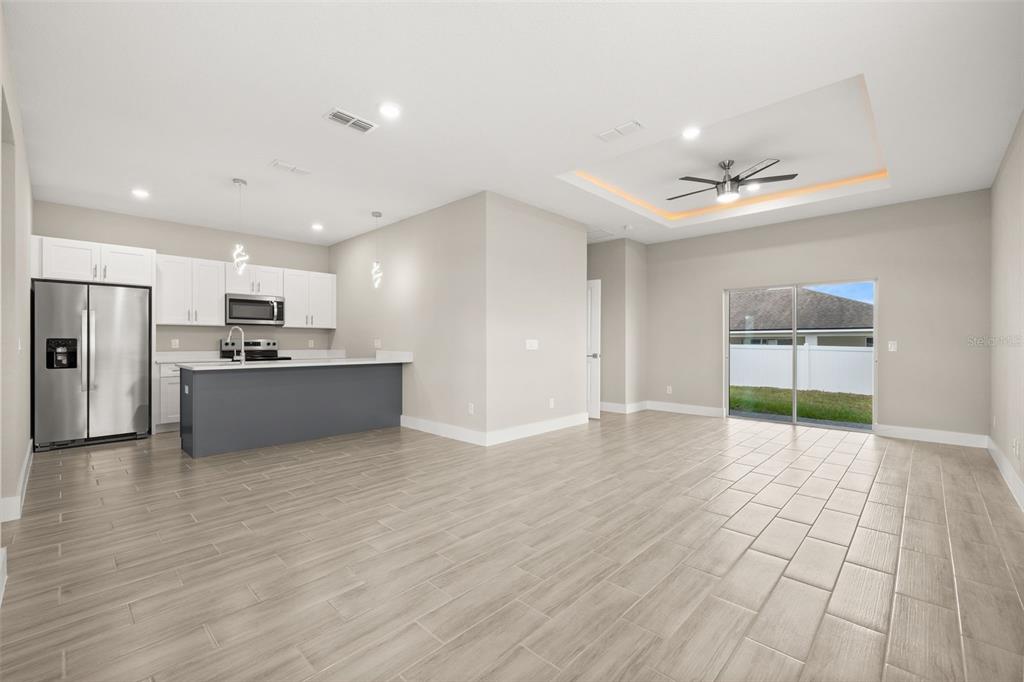 An open-concept kitchen and living area with light wood-look tile floors and a tray ceiling — 804-806 COLVILLE DRIVE, KISSIMMEE, FL