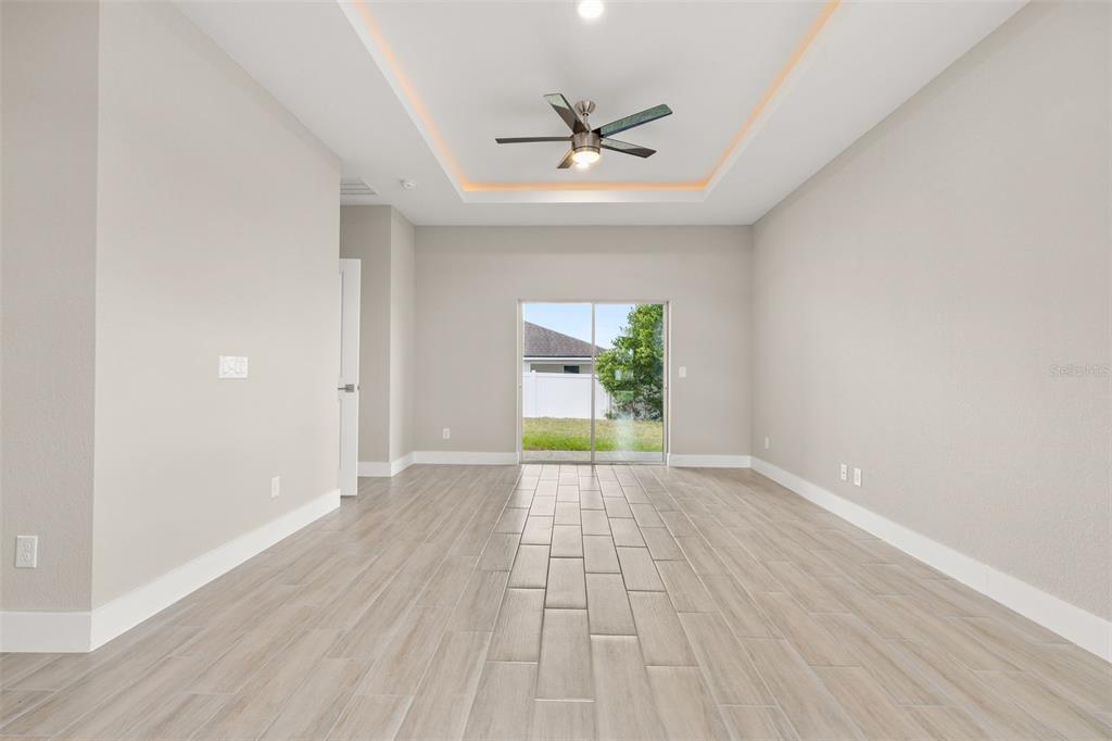 A bright, empty room features light-colored tile flooring, a tray ceiling with a fan, and sliding doors — 804-806 COLVILLE DRIVE, KISSIMMEE, FL