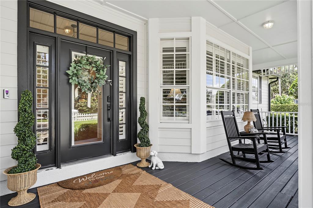A covered front porch features a black door, two rocking chairs, and a patterned rug — 1324 VIC KAY COURT, WINTER GARDEN, FL
