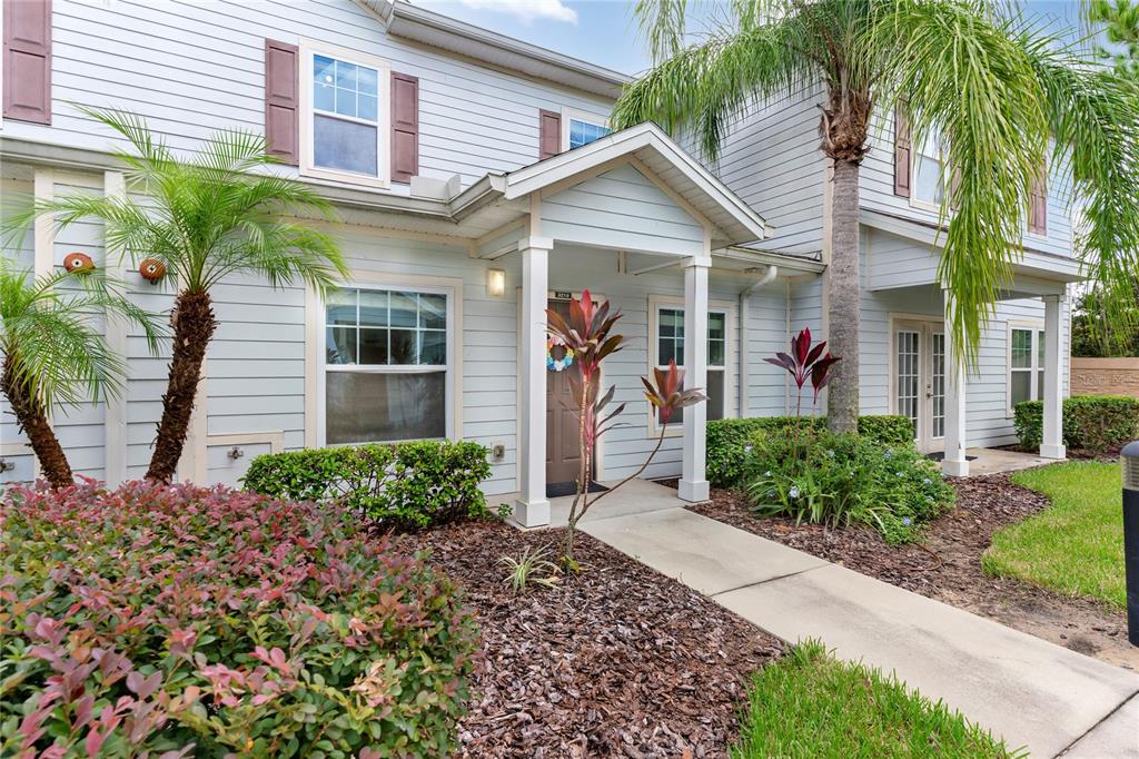 The exterior of a two-story light blue townhouse features a covered entryway and palm trees — 3210 OYSTER LANE, KISSIMMEE, FL