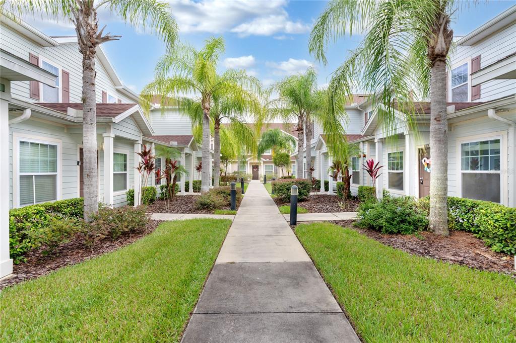 A concrete walkway leads between two rows of light-colored townhouses lined with palm trees — 3210 OYSTER LANE, KISSIMMEE, FL