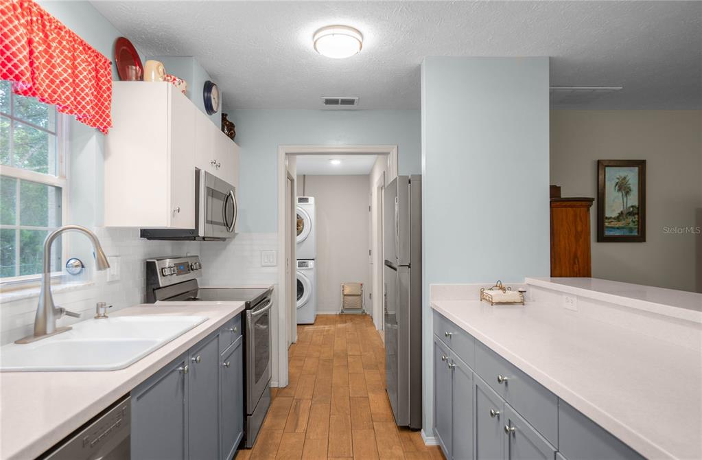 A kitchen features grey lower cabinets, white upper cabinets, stainless steel appliances, and wood-look flooring — 10407 S DREW BRYANT CIRCLE, FLORAL CITY, FL