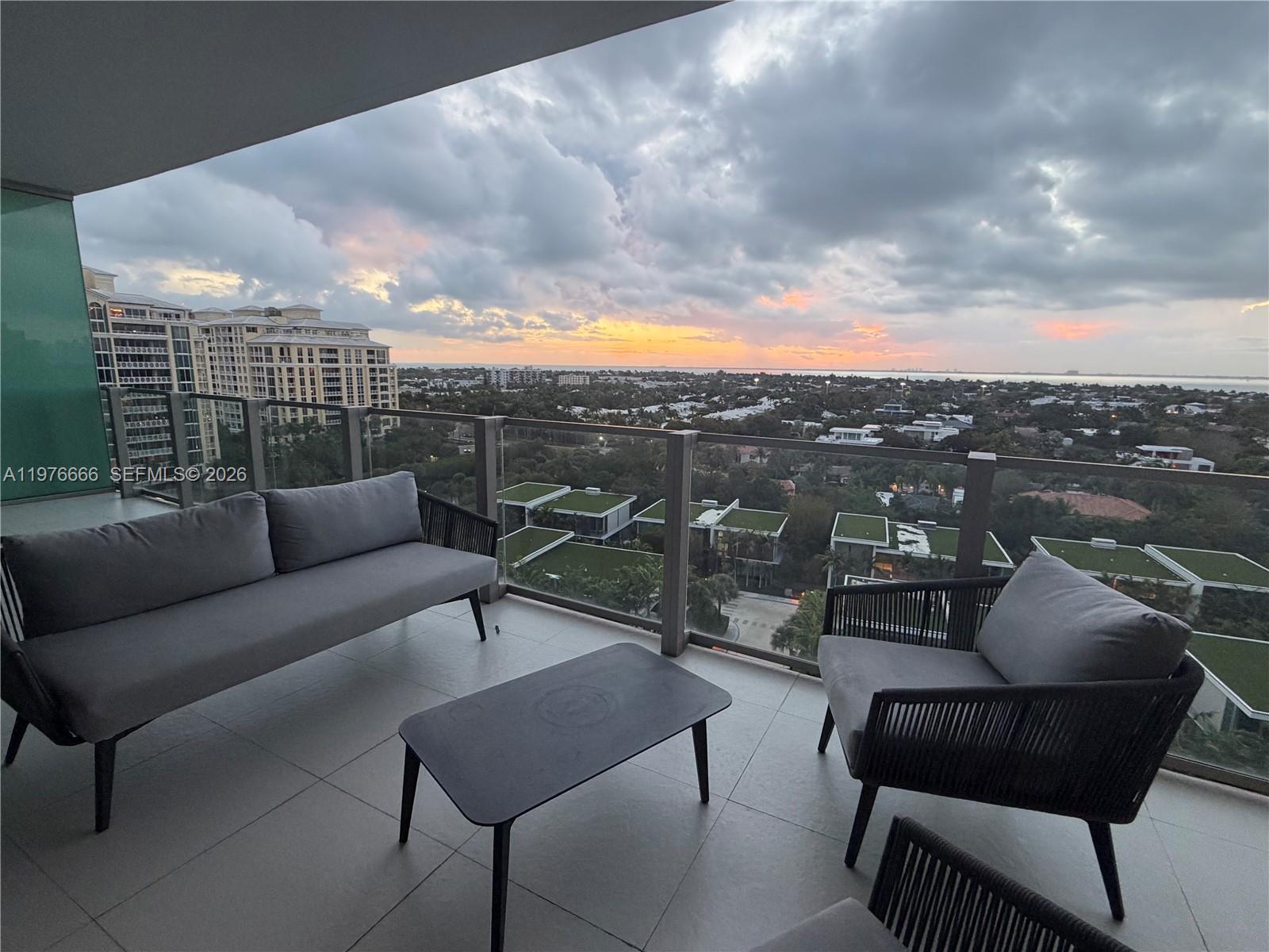 A balcony features modern outdoor furniture overlooking a suburban landscape under a cloudy sunset sky — 350 Ocean Dr # 1105N, Key Biscayne FL 33149, KEY BISCAYNE, FL
