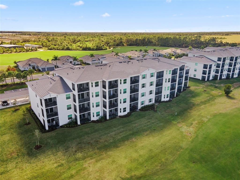 An aerial view shows a multi-story apartment building situated next to a golf course — 12240 WELLEN GOLF STREET UNIT 104, VENICE, FL