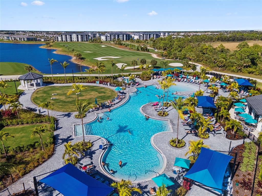 An aerial view shows a large resort-style swimming pool with palm trees and lounge chairs — 12240 WELLEN GOLF STREET UNIT 104, VENICE, FL