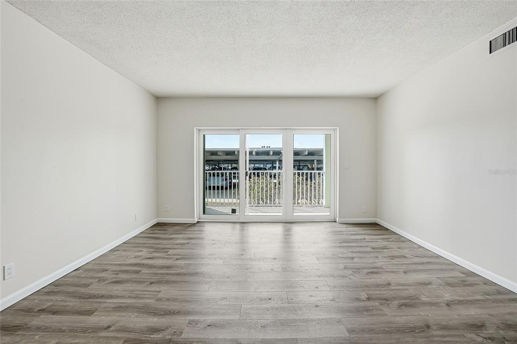 An empty room with light-colored walls, wood-look flooring, and a sliding glass door to a balcony — 420 64TH AVENUE UNIT 107, ST PETE BEACH, FL