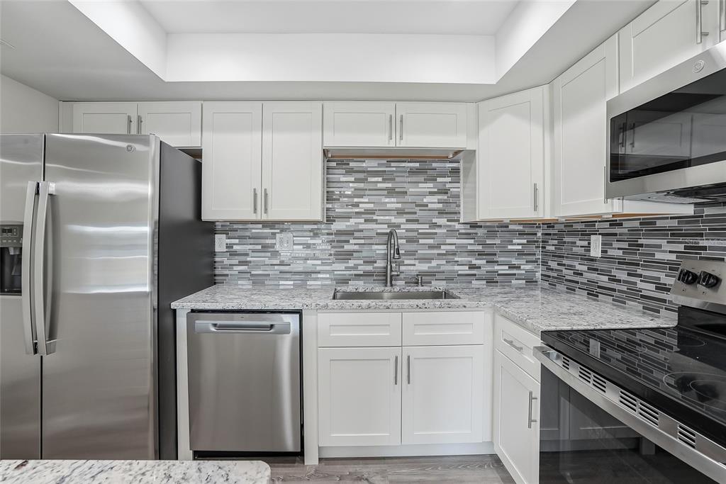 A kitchen features white cabinets, stainless steel appliances, granite countertops, and a gray tiled backsplash — 420 64TH AVENUE UNIT 107, ST PETE BEACH, FL