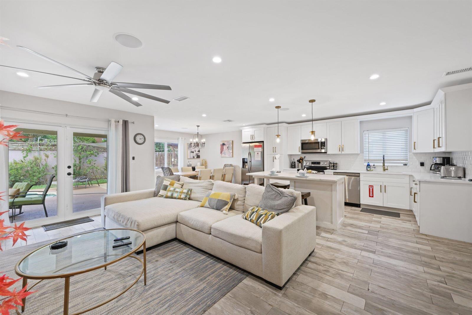 An open-concept living room and kitchen with white cabinetry, a sectional sofa, and glass doors — 513 Curlew Road, Delray Beach FL 33444, DELRAY BEACH, FL