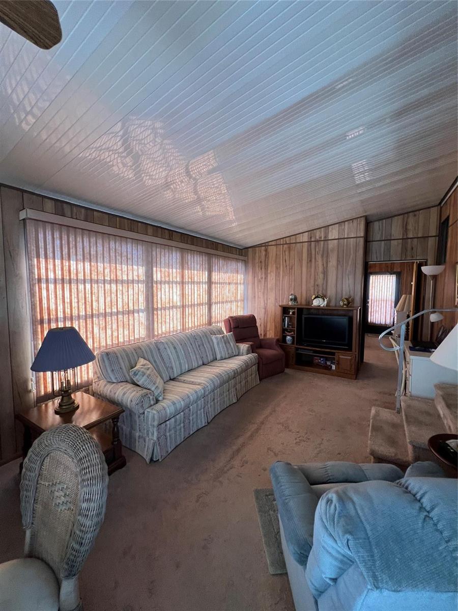 A living room features wood-paneled walls, a vaulted ceiling, a striped sofa, and carpeted floors — 6494 SE 54th Lane, Okeechobee FL 34974, OKEECHOBEE, FL