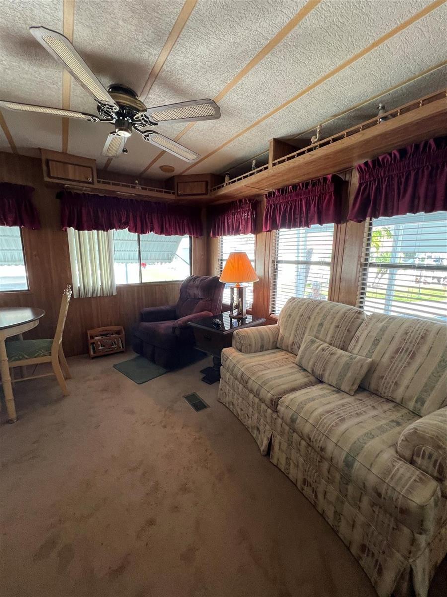 A living room features wood-paneled walls, a patterned sofa, a recliner, and a ceiling fan — 6494 SE 54th Lane, Okeechobee FL 34974, OKEECHOBEE, FL