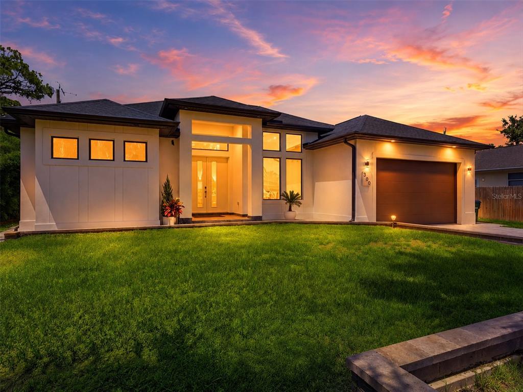 A modern single-story house with a white exterior, dark roof, and attached garage at sunset — 380 COWRY ROAD, VENICE, FL