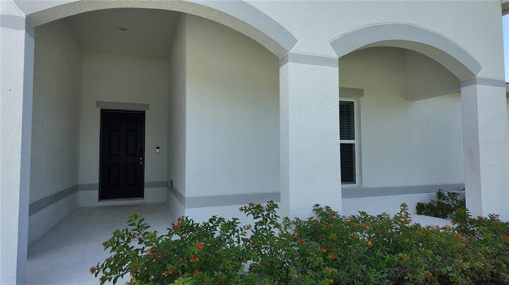 A covered entryway with a dark front door and arched columns sits behind a hedge — 10000 ANTLER STREET, PORT CHARLOTTE, FL