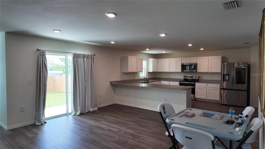 A kitchen with white cabinets and granite countertops opens to a dining area and patio — 10000 ANTLER STREET, PORT CHARLOTTE, FL
