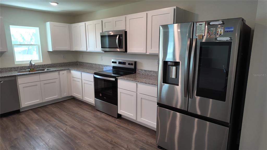 A kitchen features white cabinets, granite countertops, stainless steel appliances, and wood-look flooring — 10000 ANTLER STREET, PORT CHARLOTTE, FL