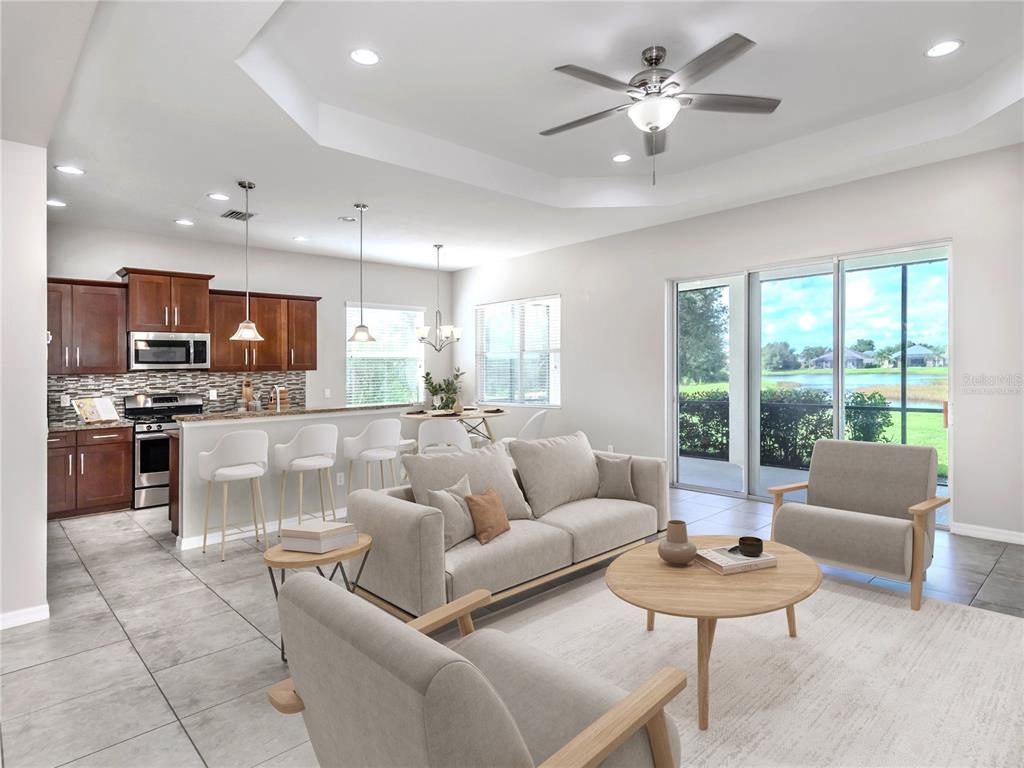 An open-concept living room and kitchen featuring light tile floors, neutral furniture, and sliding doors — 11406 BELVEDERE TERRACE, BRADENTON, FL