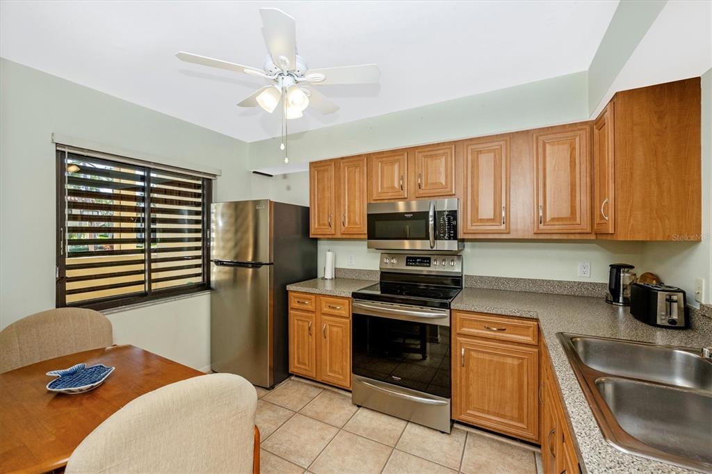 A kitchen features wood cabinets, stainless steel appliances, tile flooring, and an adjacent dining area — 5219 LAKE VILLAGE DRIVE UNIT 21, SARASOTA, FL