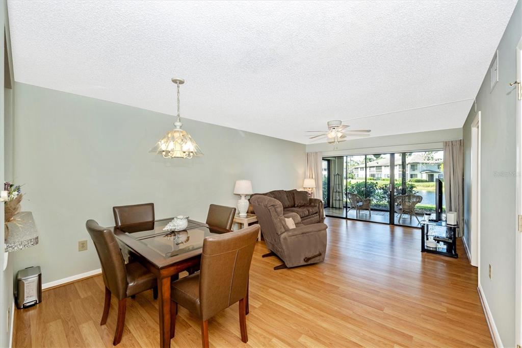A dining area and living room with wood-look flooring, a glass-top table, and sliding doors — 5219 LAKE VILLAGE DRIVE UNIT 21, SARASOTA, FL