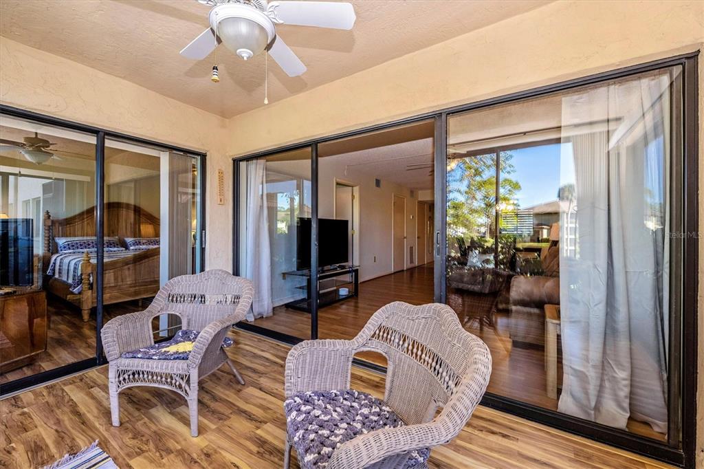 A covered patio features two wicker chairs, wood-look flooring, and sliding glass doors — 5219 LAKE VILLAGE DRIVE UNIT 21, SARASOTA, FL