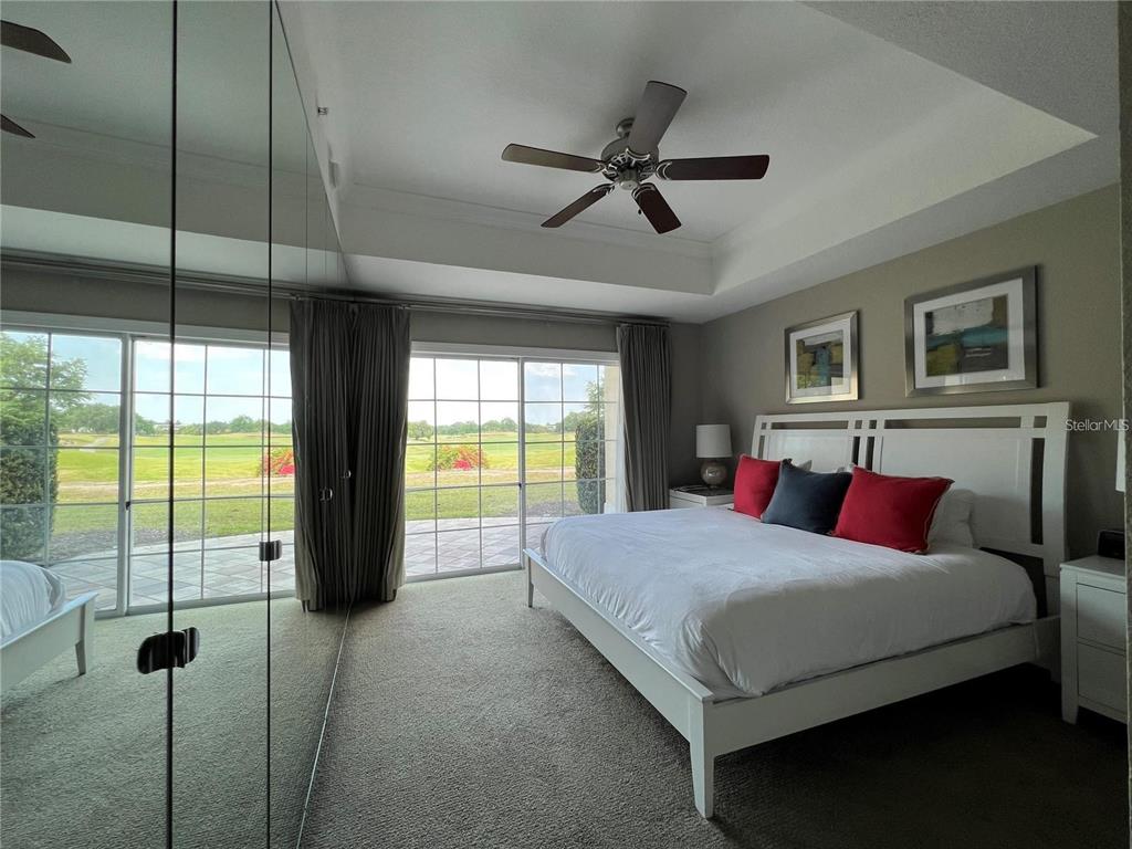 A bedroom features a white bed, mirrored closet doors, and sliding glass doors overlooking a golf course — 1301 SEVEN EAGLES COURT UNIT 1301, REUNION, FL
