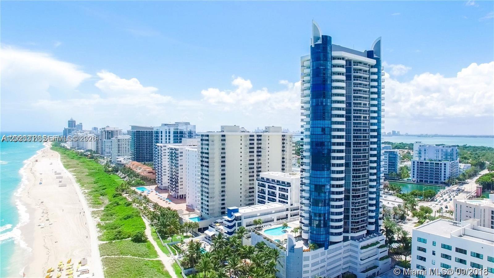 An aerial view shows a tall blue glass residential tower along a sandy beach — 6301 Collins Ave # 1206, Miami Beach FL 33141, MIAMI BEACH, FL