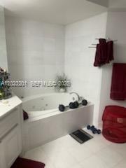 A bathroom features a white jetted tub, tiled walls, and red towels on a rack — 6301 Collins Ave # 1206, Miami Beach FL 33141, MIAMI BEACH, FL